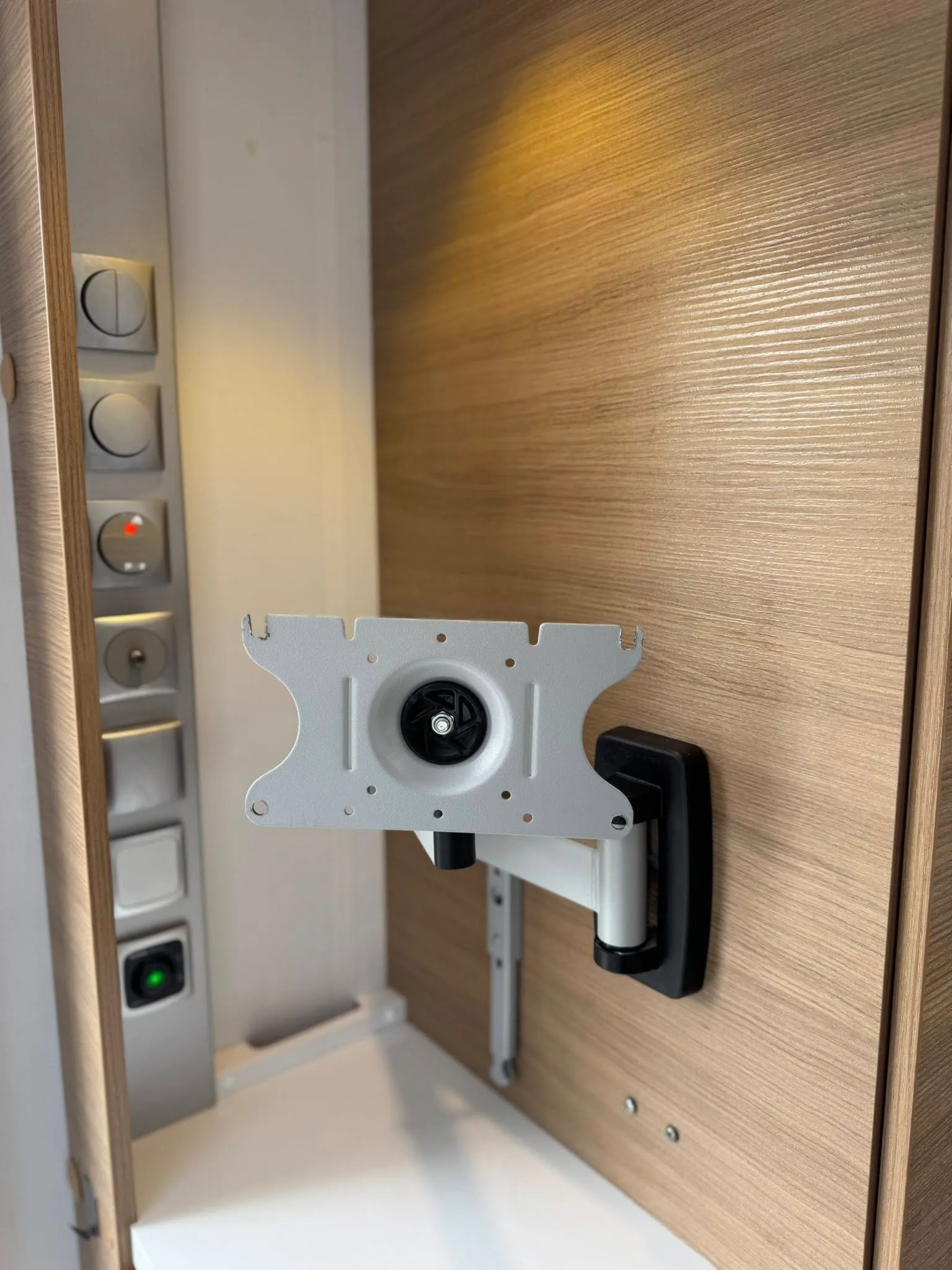 Obrázek ukazuje moderní interiér obytného vozu s držákem pro televizi a ovládacími prvky.