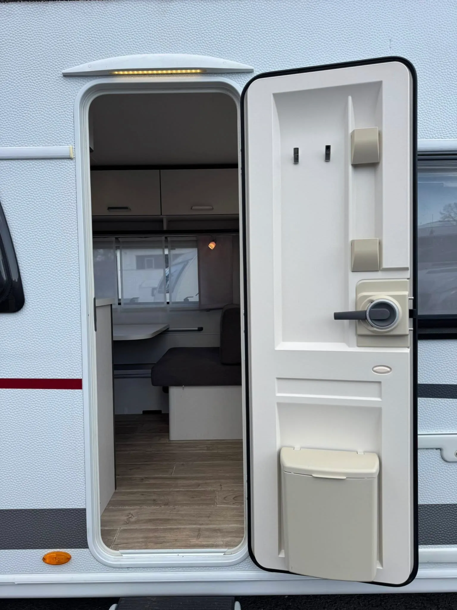 Kouzelné útulné místo v karavanu s otevřenými dveřmi, připravené na dobrodružství a relaxaci.