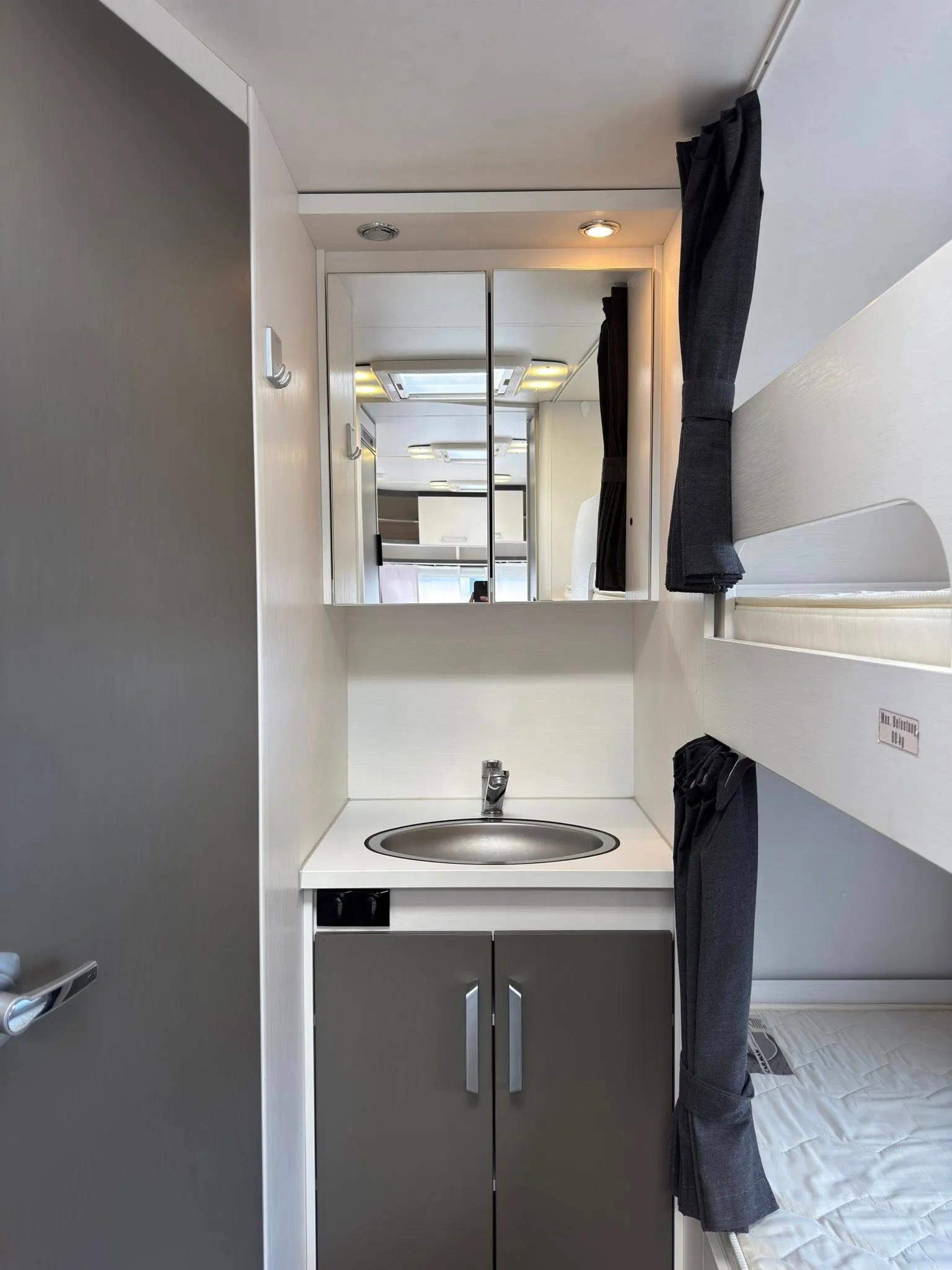 Obrázek interiéru moderního karavanu s kuchyňským koutem a úložnými prostory. Elegantní design a funkčnost.