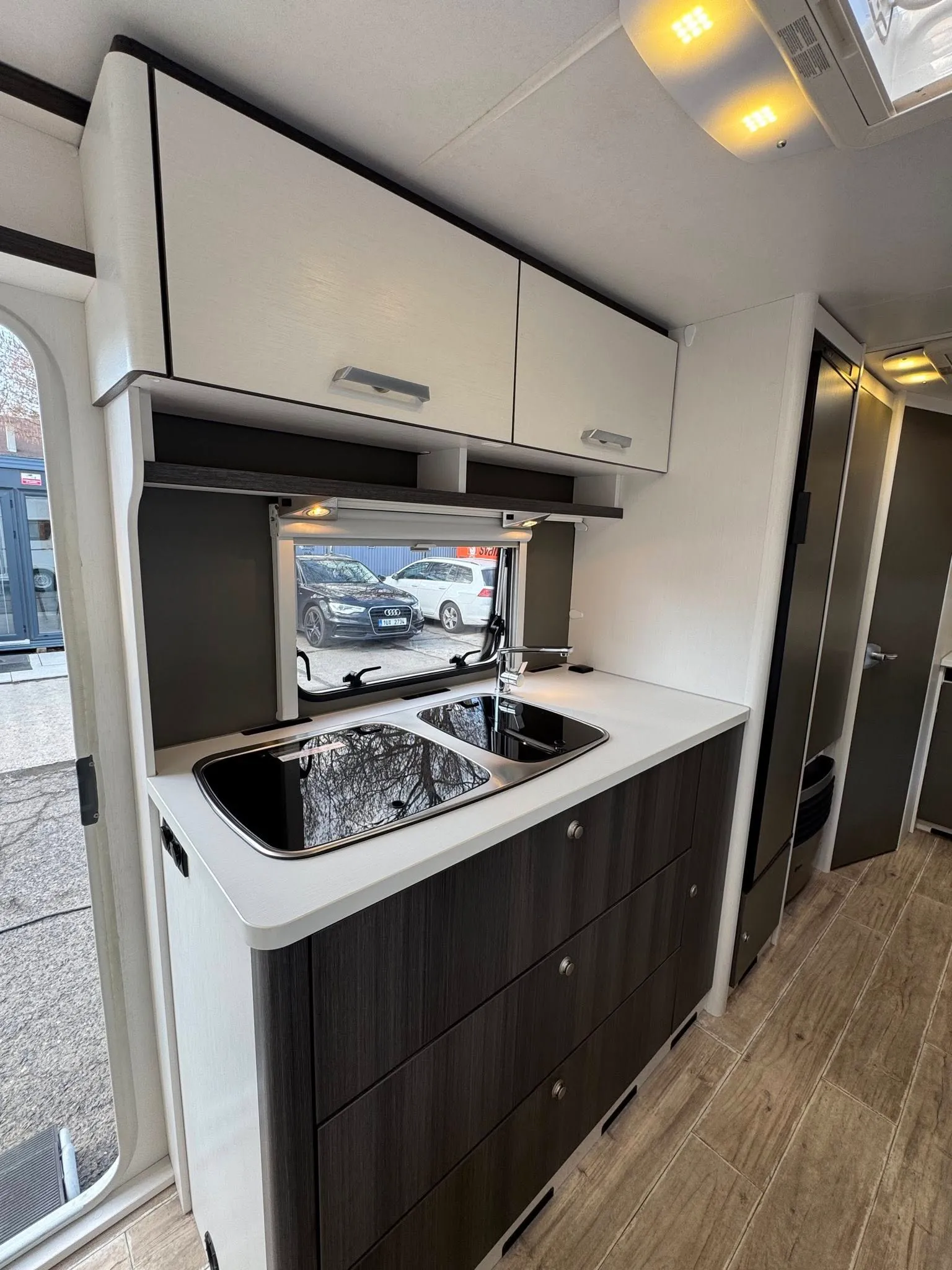 Obrázek interiéru obytného vozu, moderní kuchyňka s dřezem a úložnými prostory. Stylový design pro pohodlí.