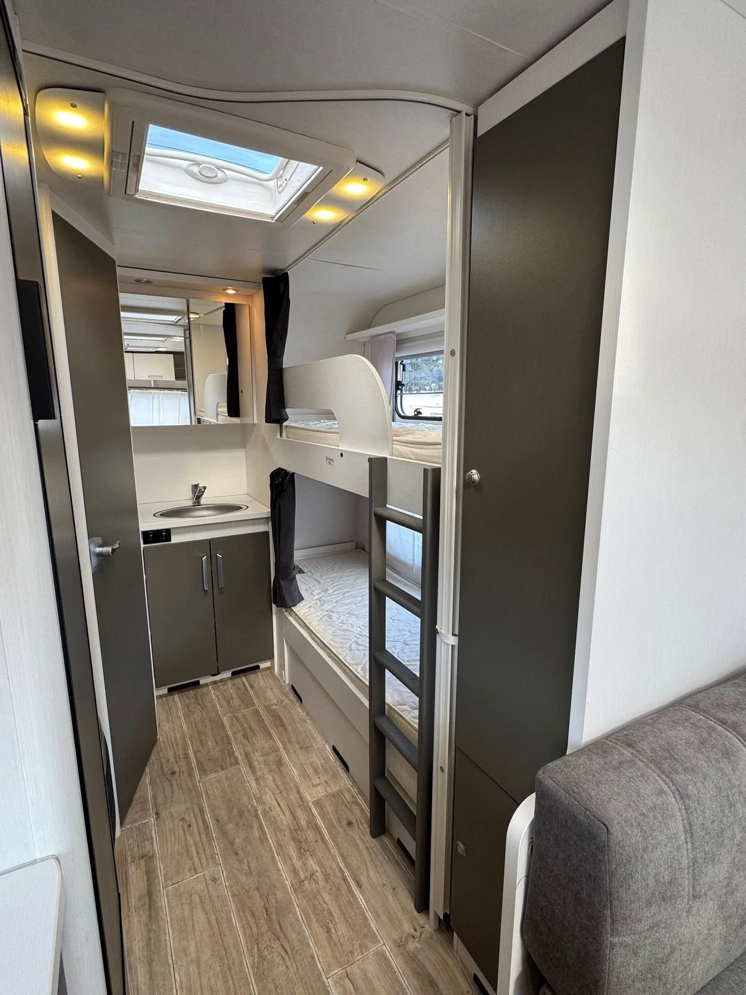 Obrázek interiéru karavanu s praktickým uspořádáním, včetně kuchyňky a buněk na spaní.