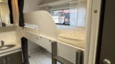 Interiér karavanu s patrovými postelemi a kuchyňským koutem. Ideální pro rodinné výlety a pohodlné spaní.