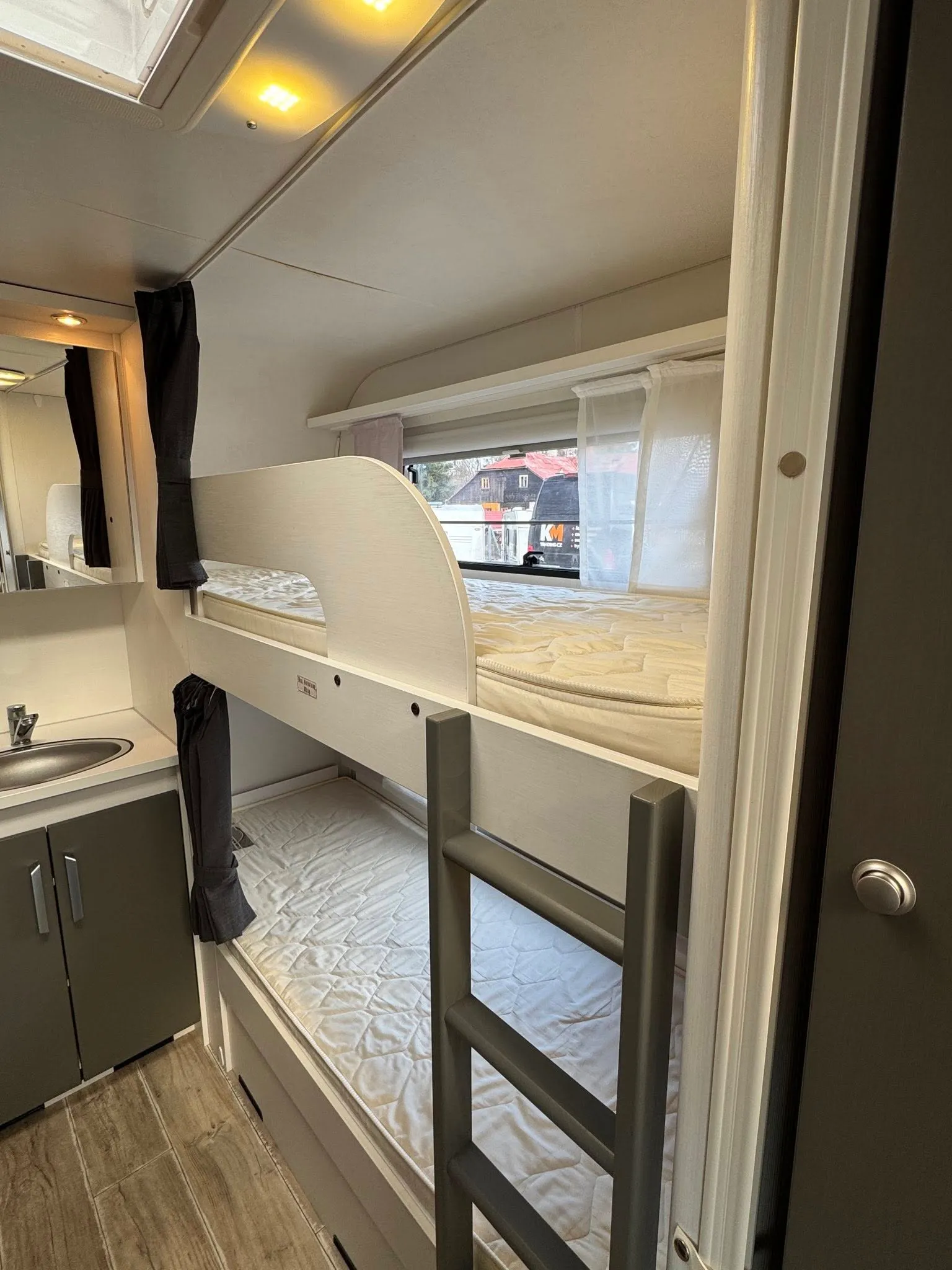 Interiér karavanu s patrovými postelemi a kuchyňským koutem. Ideální pro rodinné výlety a pohodlné spaní.