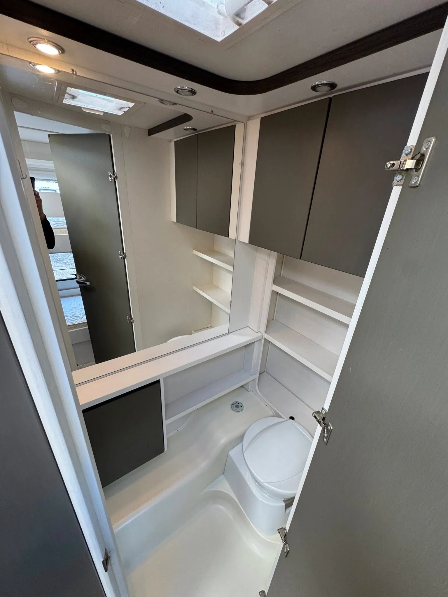 Obrázek interiéru ukazuje moderní koupelnu v obytném autě s úložným prostorem a toaletou.