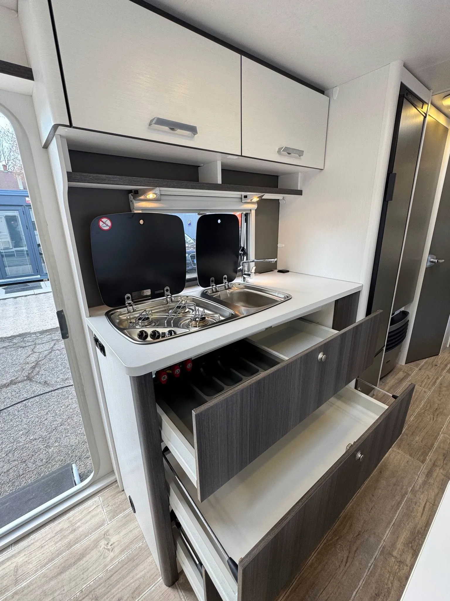 Moderní kuchyně v karavanu s dřezem a úložnými prostory, ideální pro kempování a cestování.