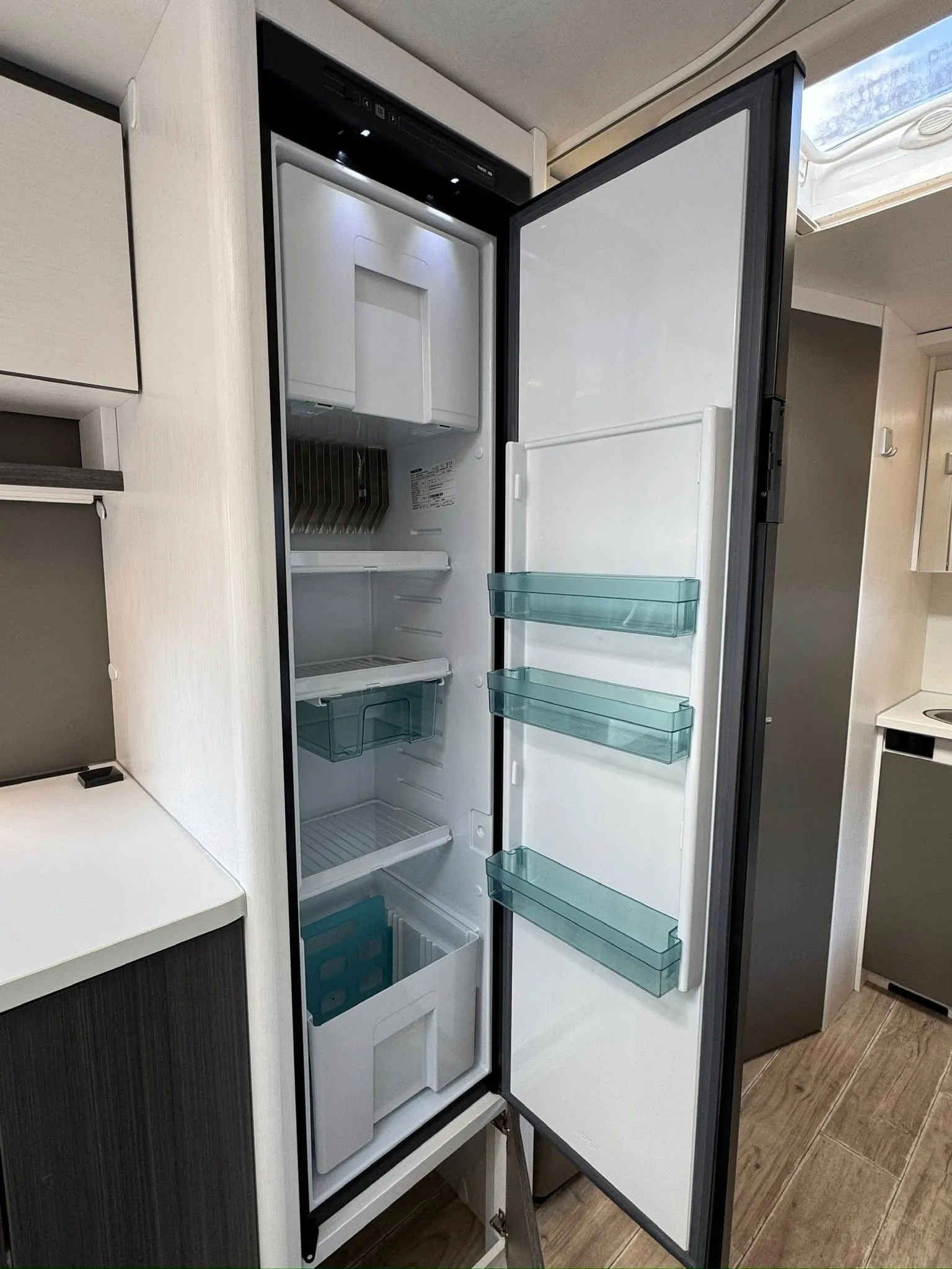 Obrázek zobrazuje chladničku uvnitř obytného vozu, ideální pro skladování potravin na cestách.