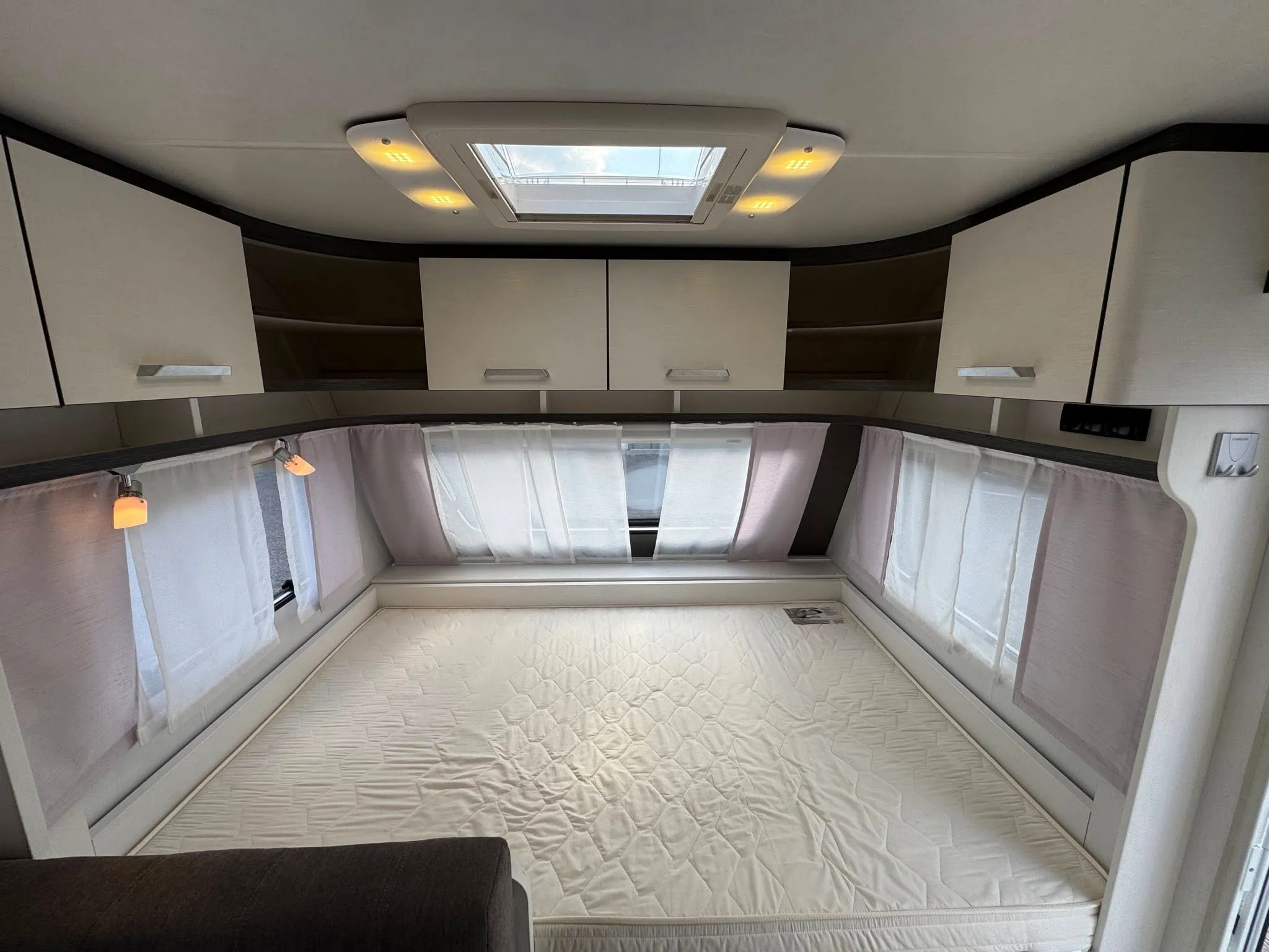 Interiér karavanu s pohodlným spacím prostorem a úložnými skříněmi. Ideální pro pohodové cestování.