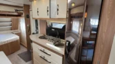 Obrázek interiéru karavanu s kuchyňským koutem a pohodlným sezením. Moderní design a dostatek úložného prostoru.