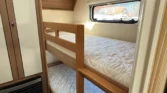 Obrázek interiéru karavanu s patrovou postelí a úložným prostorem. Moderní a prostorný.