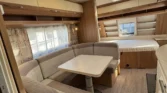 Interiér karavanu s pohodlným posezením a stolečkem. Moderní a prostorné uspořádání pro příjemný pobyt.