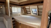 Interiér karavanu, příjemný a prostorný s velkým lůžkem a úložnými prostory, ideální pro pohodlné cestování.
