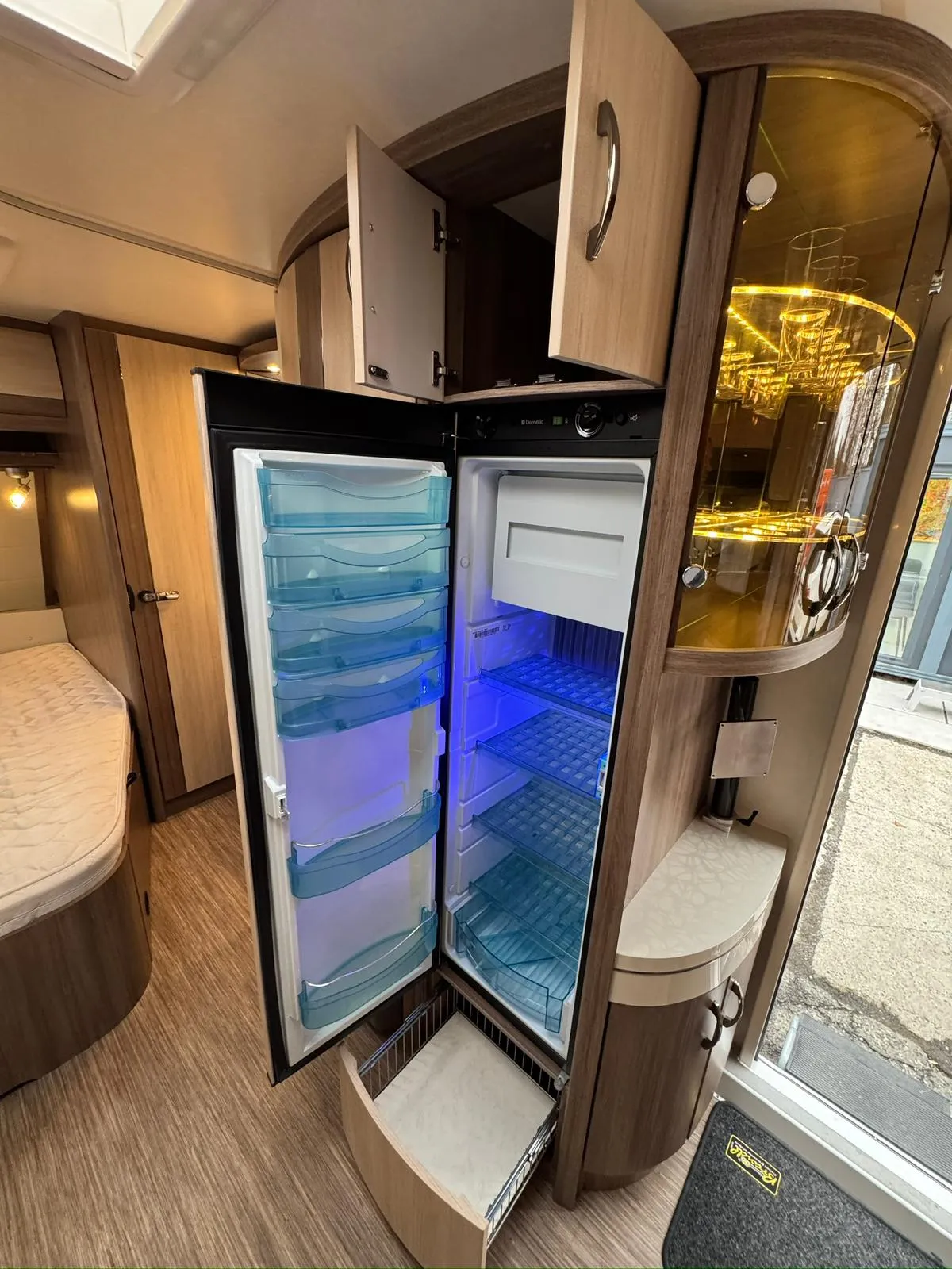 Interiér obytného auta s moderní lednicí a skříňkami, ideální pro pohodlné cestování a kempování.