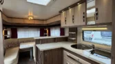 Obrázek zobrazuje moderní interiér karavanu s kuchyňským koutem, úložným prostorem a pohodlným posezením.