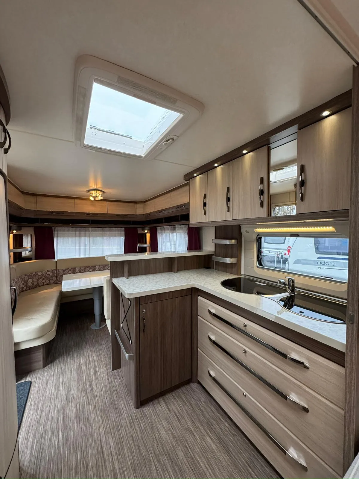 Obrázek zobrazuje moderní interiér karavanu s kuchyňským koutem, úložným prostorem a pohodlným posezením.