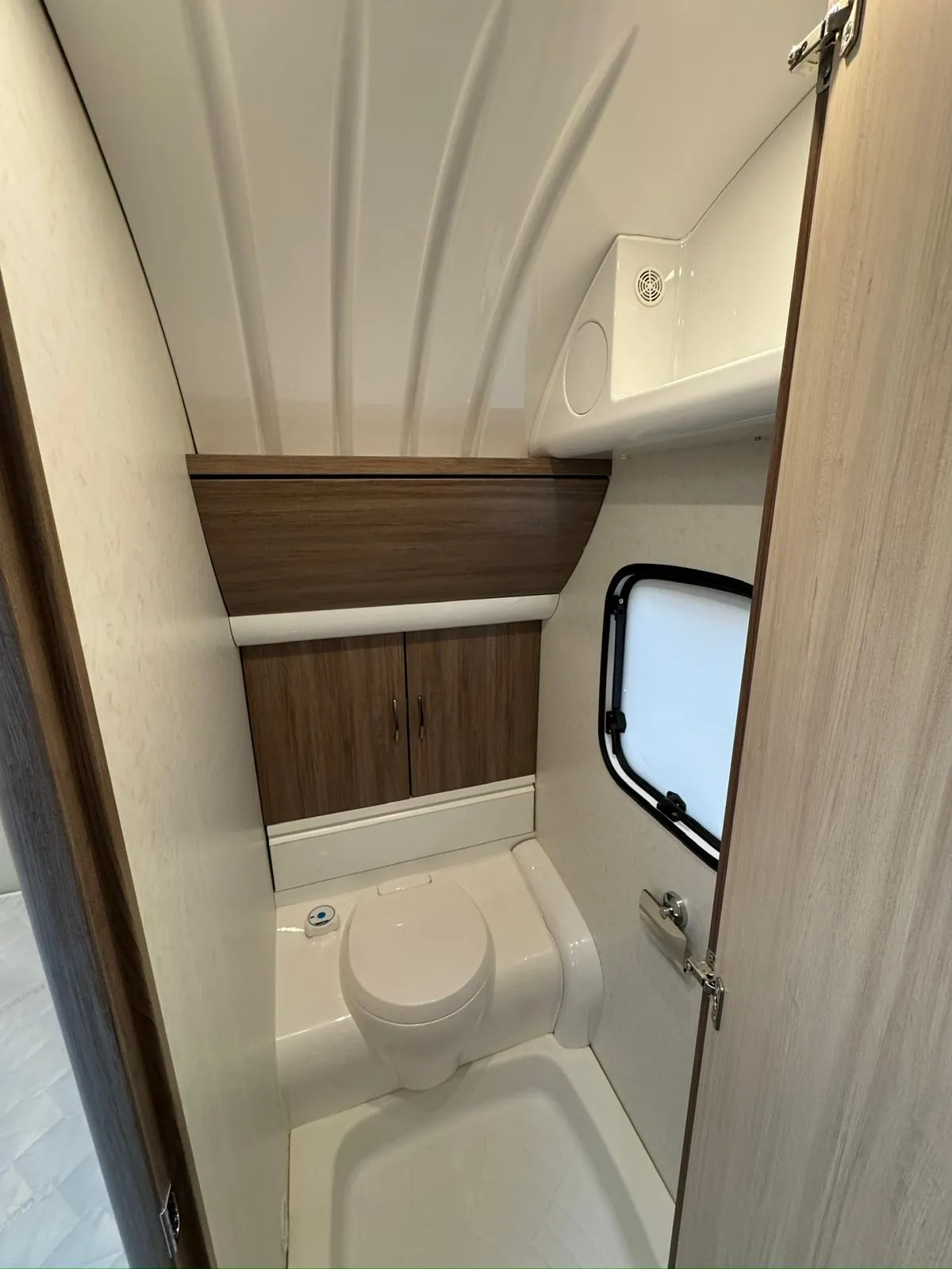 Koupelna v karavanu s toaletou, skříňkami a oknem. Moderní design pro pohodlí při cestování.