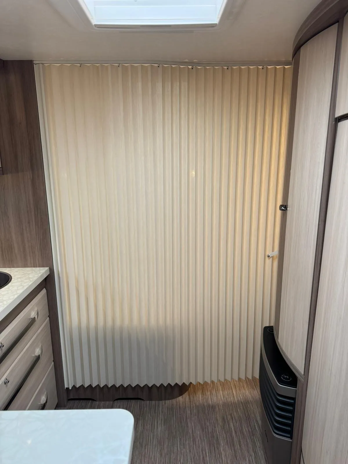 Interiér obytného vozu s moderním designem a roletami. Vybavení zahrnuje kuchyňku a úložné prostory.