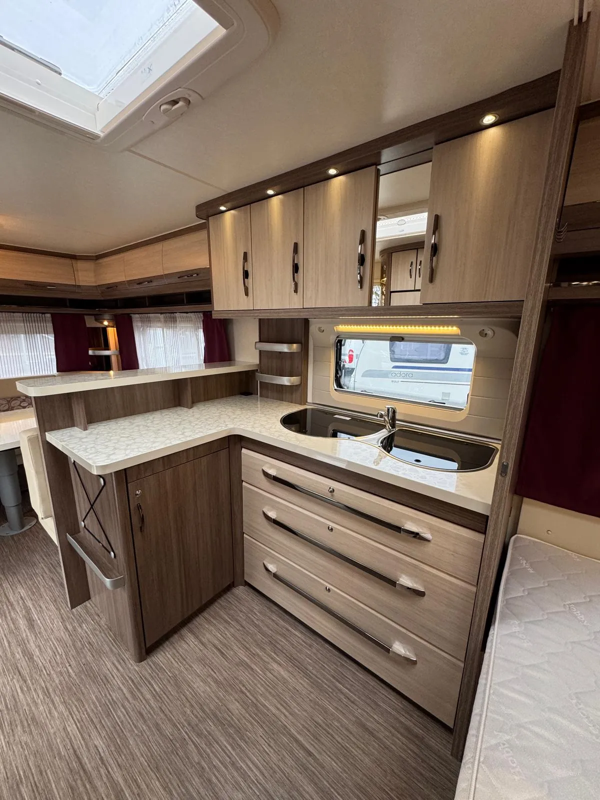 Moderní interiér karavanu s kuchyňským koutem, skříňkami a příjemným osvětlením. Ideální pro pohodlné cestování.