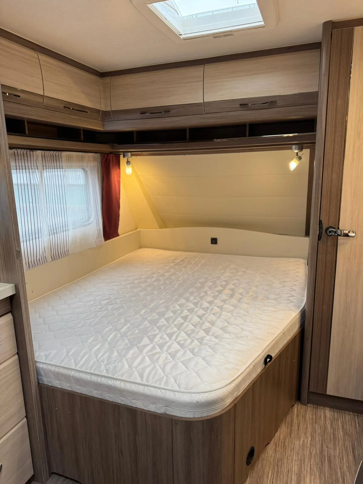 Obrázek ukazuje interiér karavanu s prostornou postelí a úložnými skrínkami. Ideální pro pohodlné cestování.