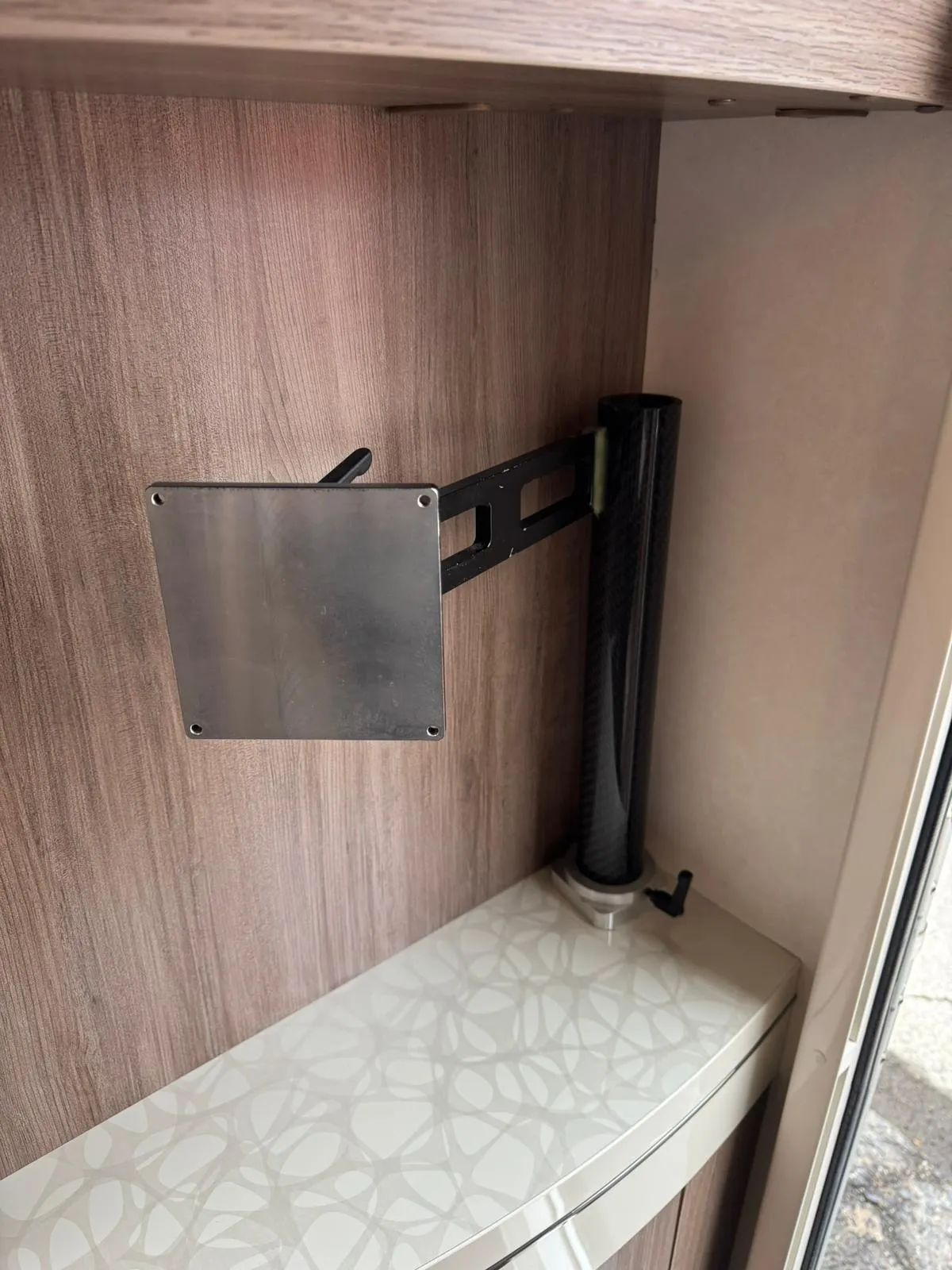 Na obrázku je interiér obytného vozu s montážním držákem a dekorativním povrchem. Model a značka nejsou viditelné.