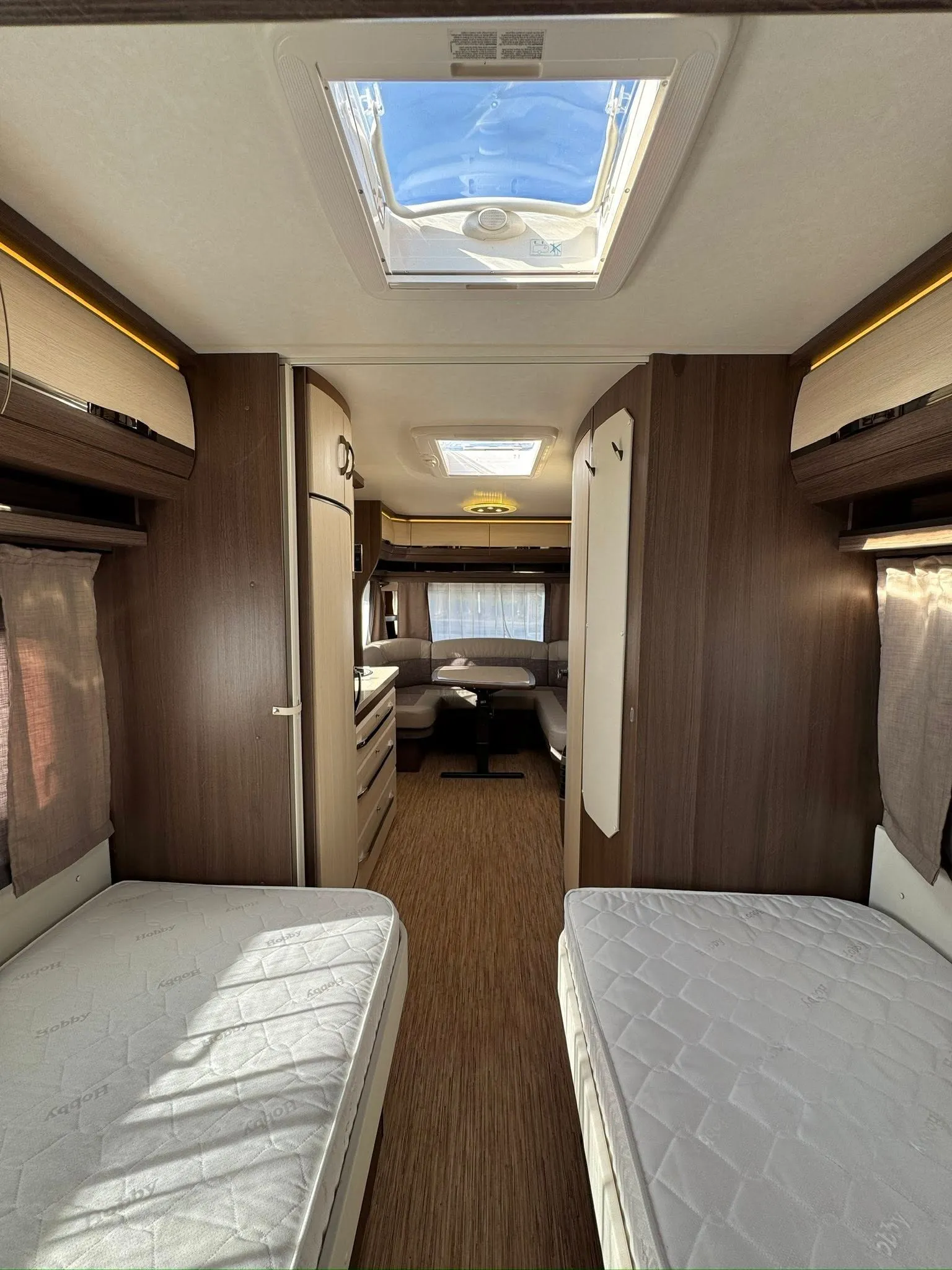 Interiér karavanu Hobby s dvěma lůžky a komfortním sezením. Ideální pro cestování s rodinou.