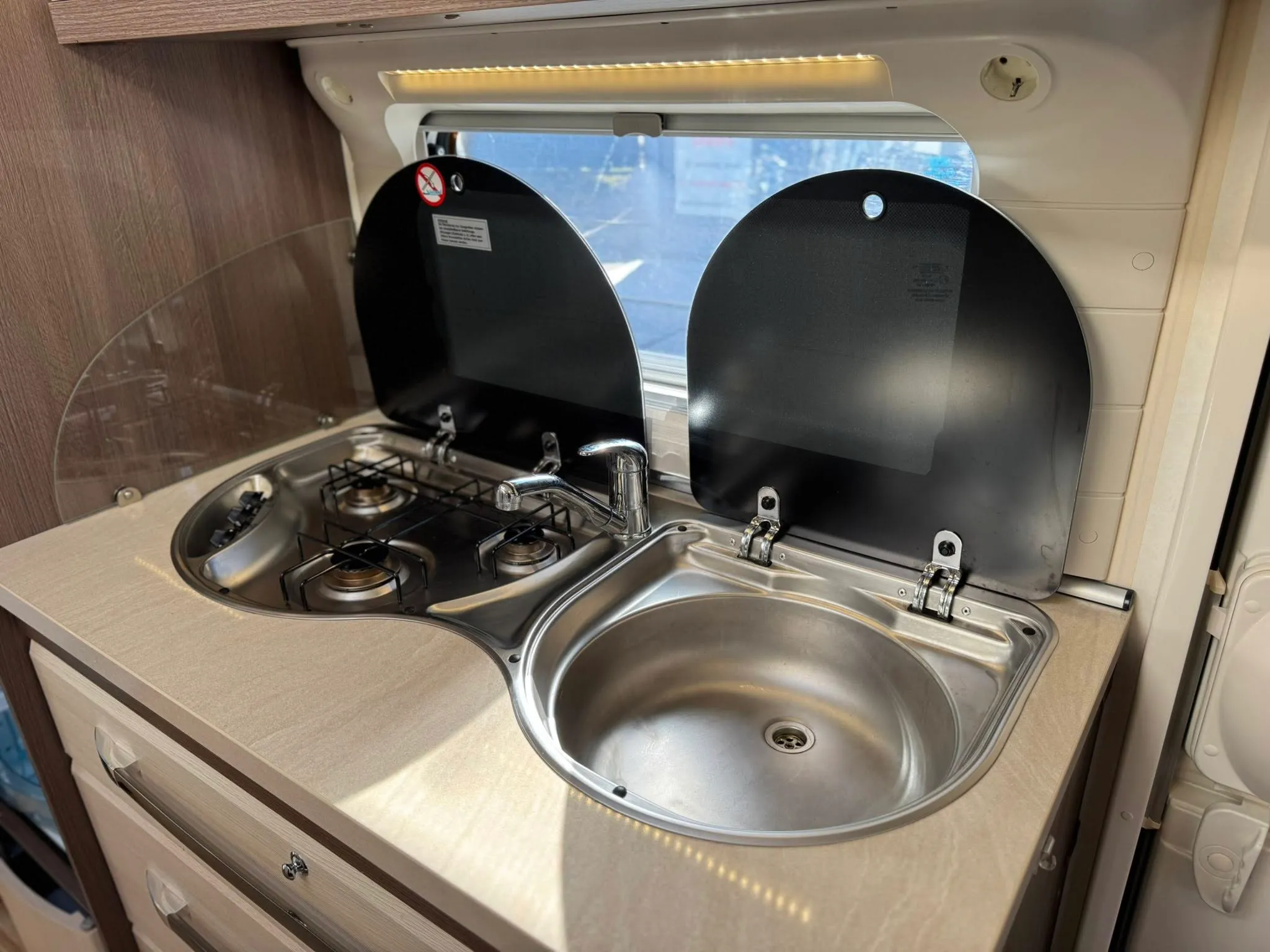 Kuchyňka obytného auta s dvouplotýnkovým vařičem a dřezem. Moderní design pro pohodlné vaření na cestách.