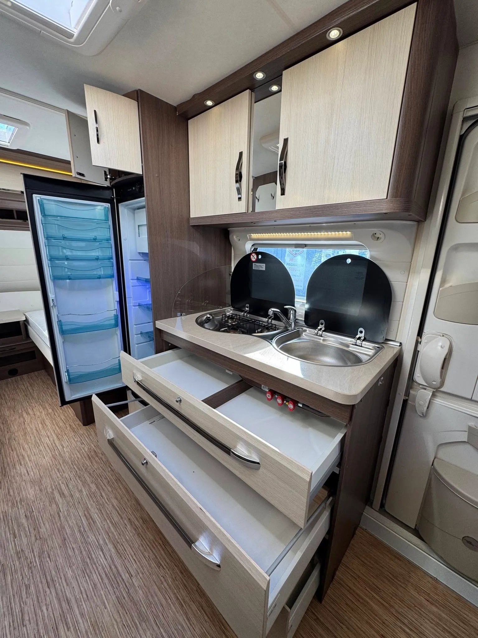 Interiér obytného auta s kuchyňskou linkou, dřezem a úložnými prostory. Moderní design pro pohodlné cestování.