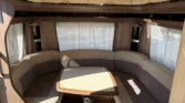 Interiér karavanu s pohodlným sezením a stolem, ideální pro relaxaci. Vzdušné prostředí s přirozeným osvětlením.