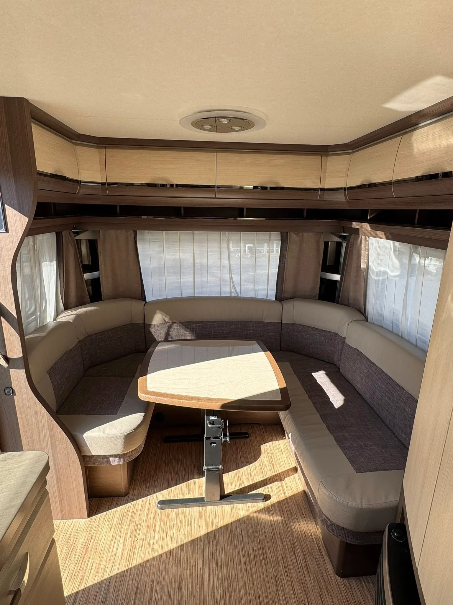 Interiér karavanu s pohodlným sezením a stolem, ideální pro relaxaci. Vzdušné prostředí s přirozeným osvětlením.