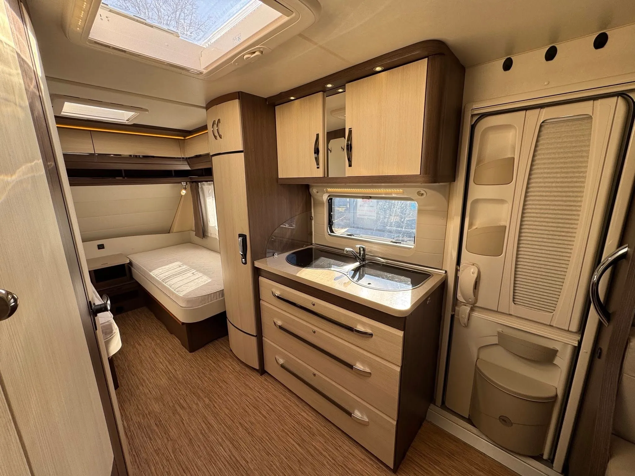 Interiér moderního karavanu s kuchyňským koutem a ložním prostorem. Prostorný a útulný pro pohodlné cestování.