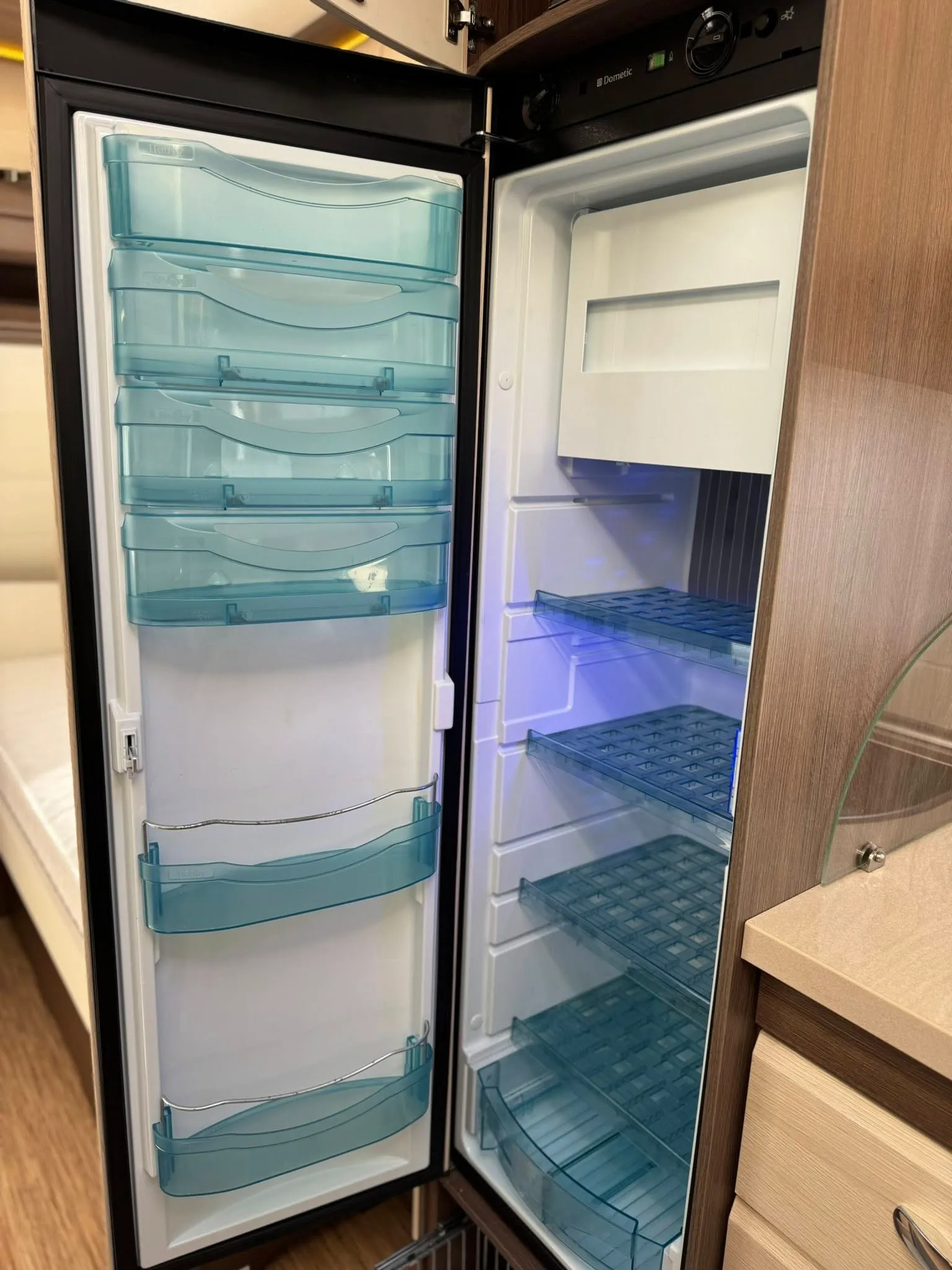 Obrázek zobrazuje lednici v obytném autě. Vnitřní prostor je dobře uspořádán s průhlednými přihrádkami.
