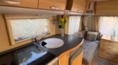 Kuchyňský kout karavanu s moderním designem, pohodlným sezením a přírodním osvětlením. Ideální pro kempování.