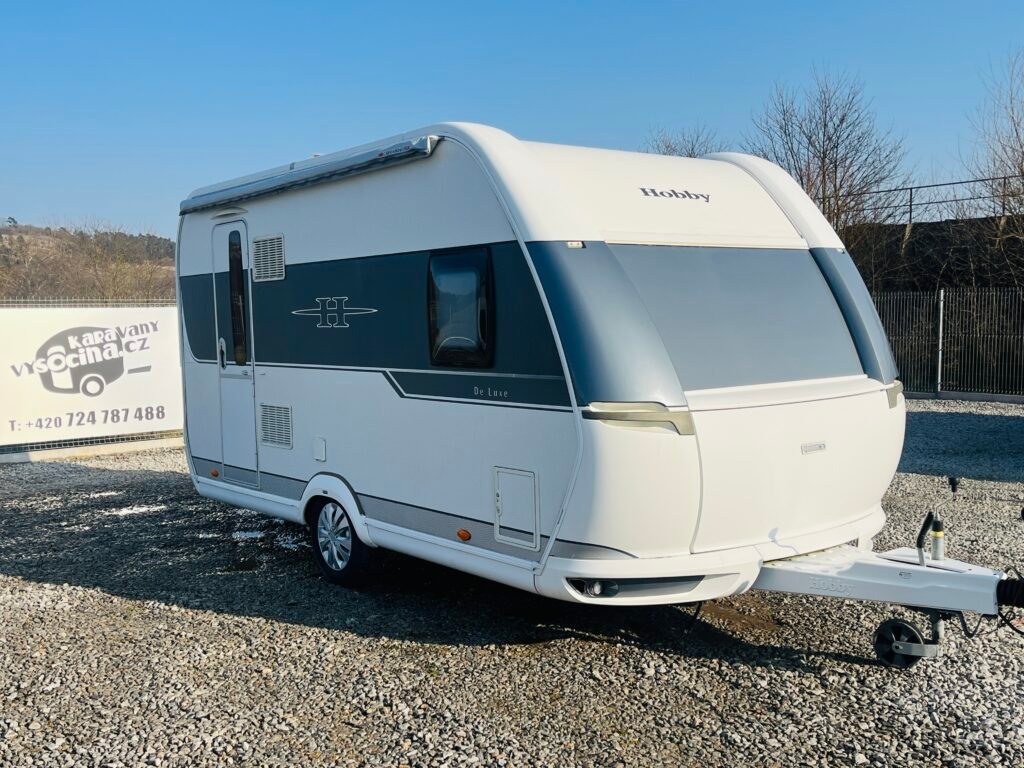 Karavan Hobby De Luxe s moderním designem a zastřešenými okny, ideální pro pohodlné cestování.