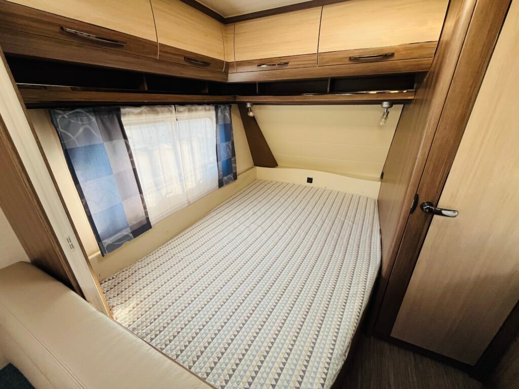 Prostorný interiér karavanu s pohodlnou postelí a úložným prostorem. Ideální pro cestování a odpočinek.