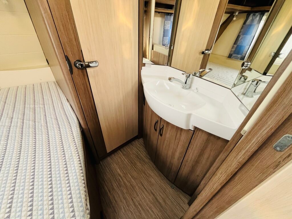 Interiér karavanu s praktickým umyvadlem a pohodlným lůžkem pro příjemný pobyt.