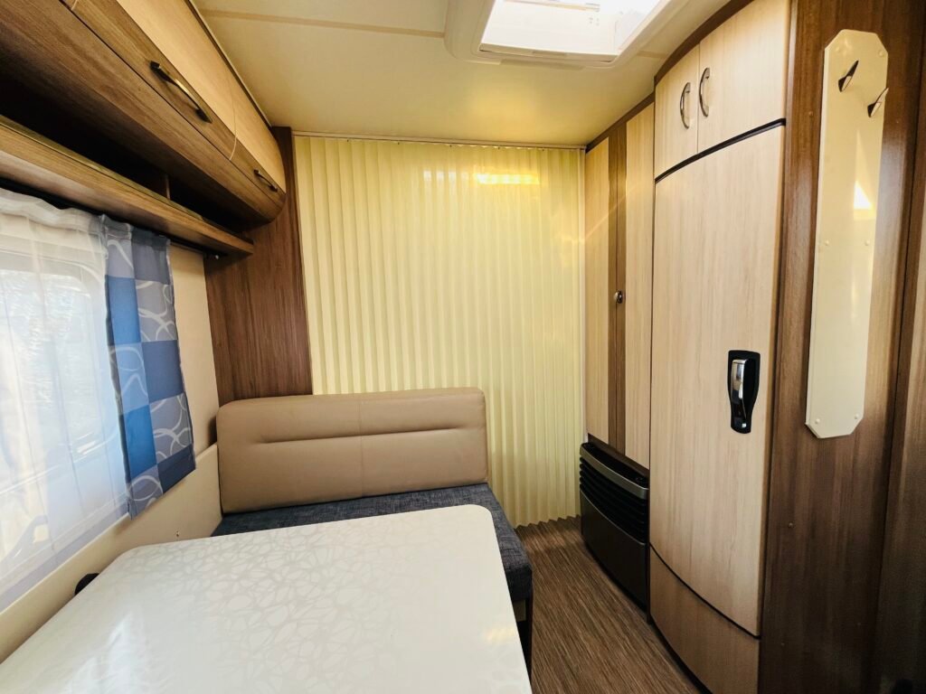 Obrázek interiéru karavanu se světlým nábytkem a pohodlným posezením. Ideální pro příjemné cestování.