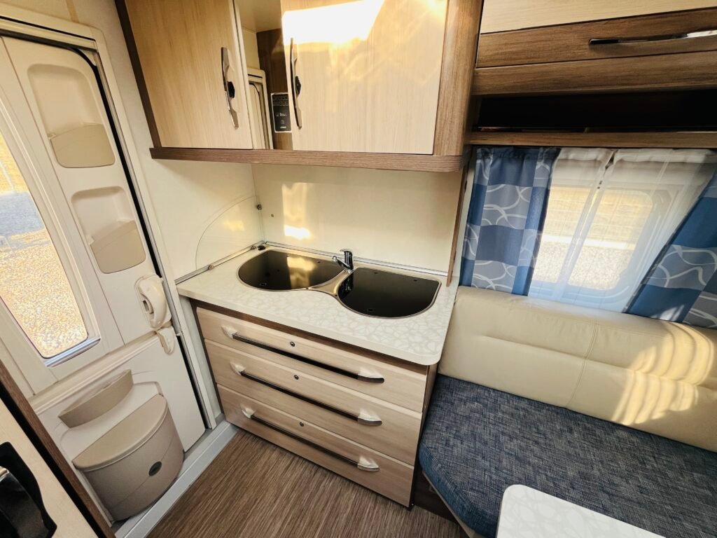 Obrázek interiéru karavanu s kuchyňským koutem a úložným prostorem. Elegantní a útulné provedení.