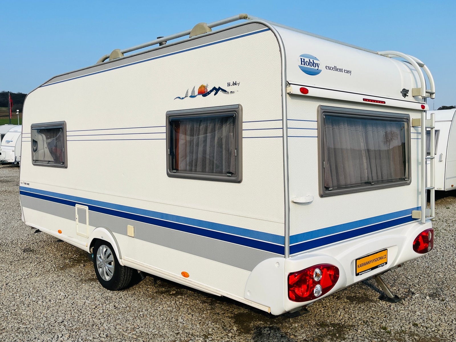 Karavan Hobby Excellent Easy s modrými pruhy, ideální pro pohodlné cestování a kempování.