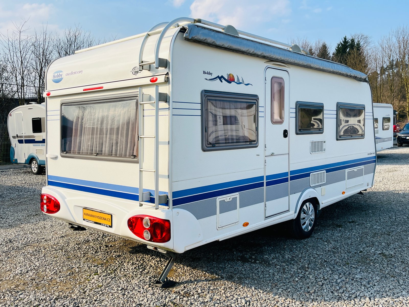 Karavan Hobby Excellent Easy s modrými pruhy, ideální pro pohodlné cestování a kempování.