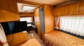 Interiér karavanu s dřevěným nábytkem, pohodlnými lůžky a televizorem. Vhodný pro pohodlné cestování.