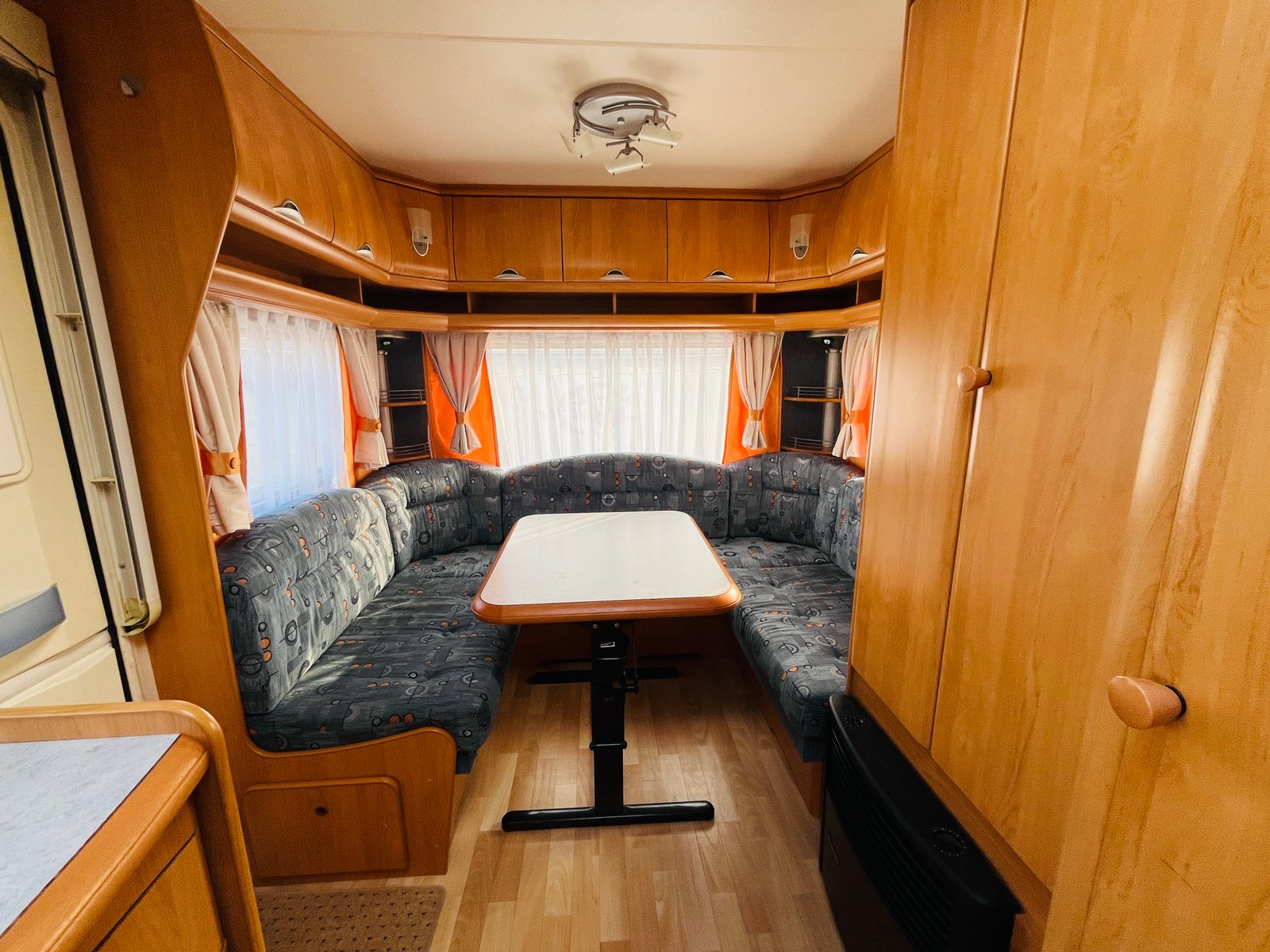 Interiér karavanu s pohodlným posezením a stolem, ideální pro rodinné výlety. Dřevěné prvky a útulná atmosféra.