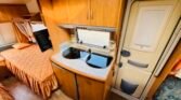 Interiér karavanu Hobby, zahrnující kuchyňku a ložko s příjemnou výzdobou. Ideální pro dobrodružství na cestách.
