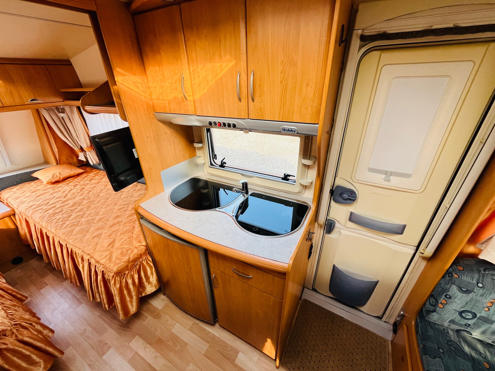 Interiér karavanu Hobby, zahrnující kuchyňku a ložko s příjemnou výzdobou. Ideální pro dobrodružství na cestách.