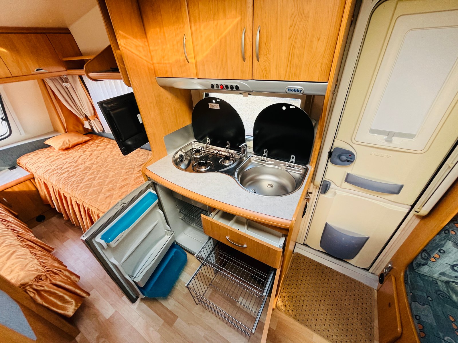 Interiér karavanu Hobby s kuchyňkou a ložnicí. Pohodlný prostor pro relaxaci a vaření na cestách.