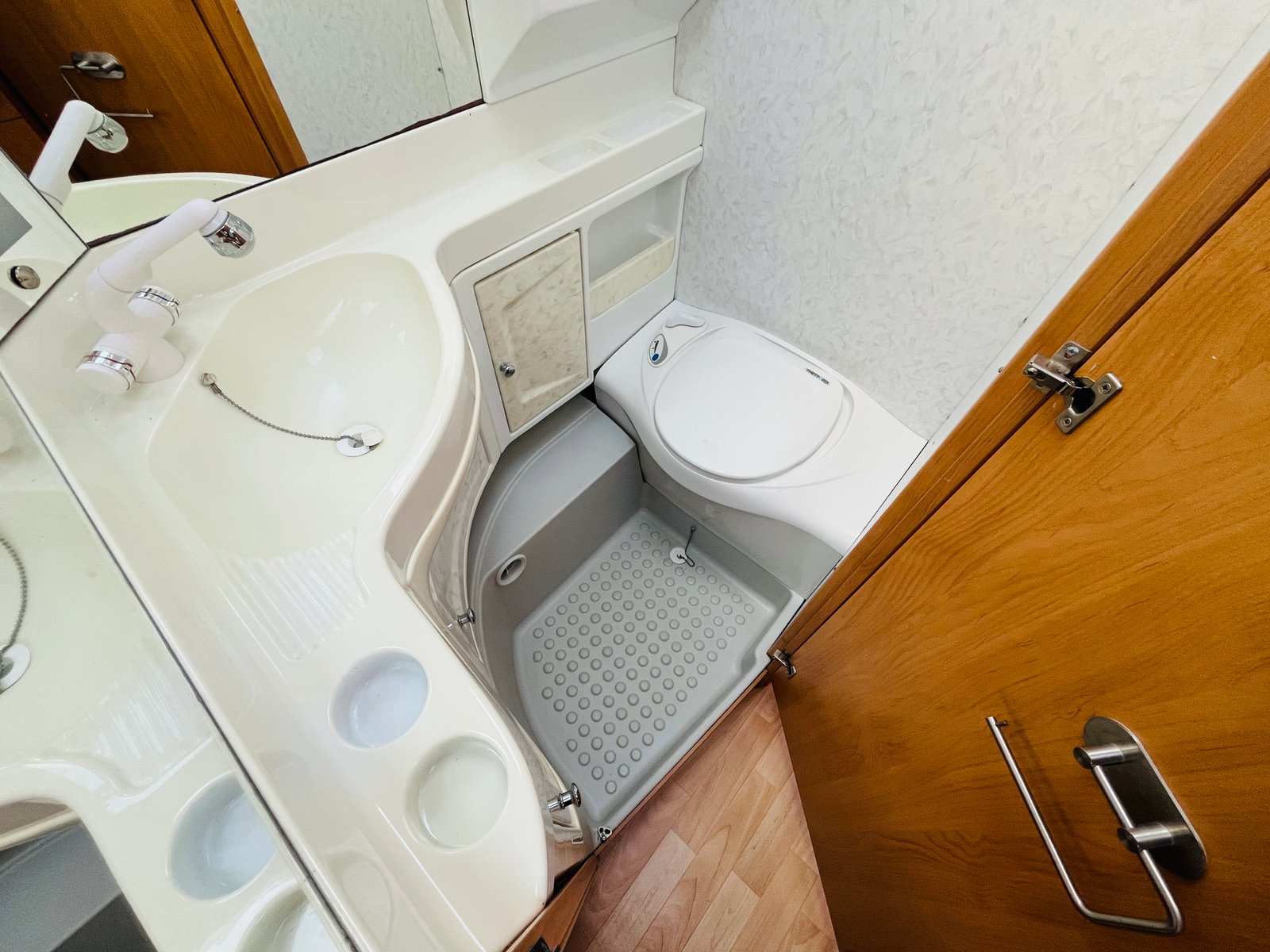 Obrázek interiéru obytného vozu s koupelnou, obsahuje umyvadlo a toaletu. Pro pohodlné cestování na dovolenou.