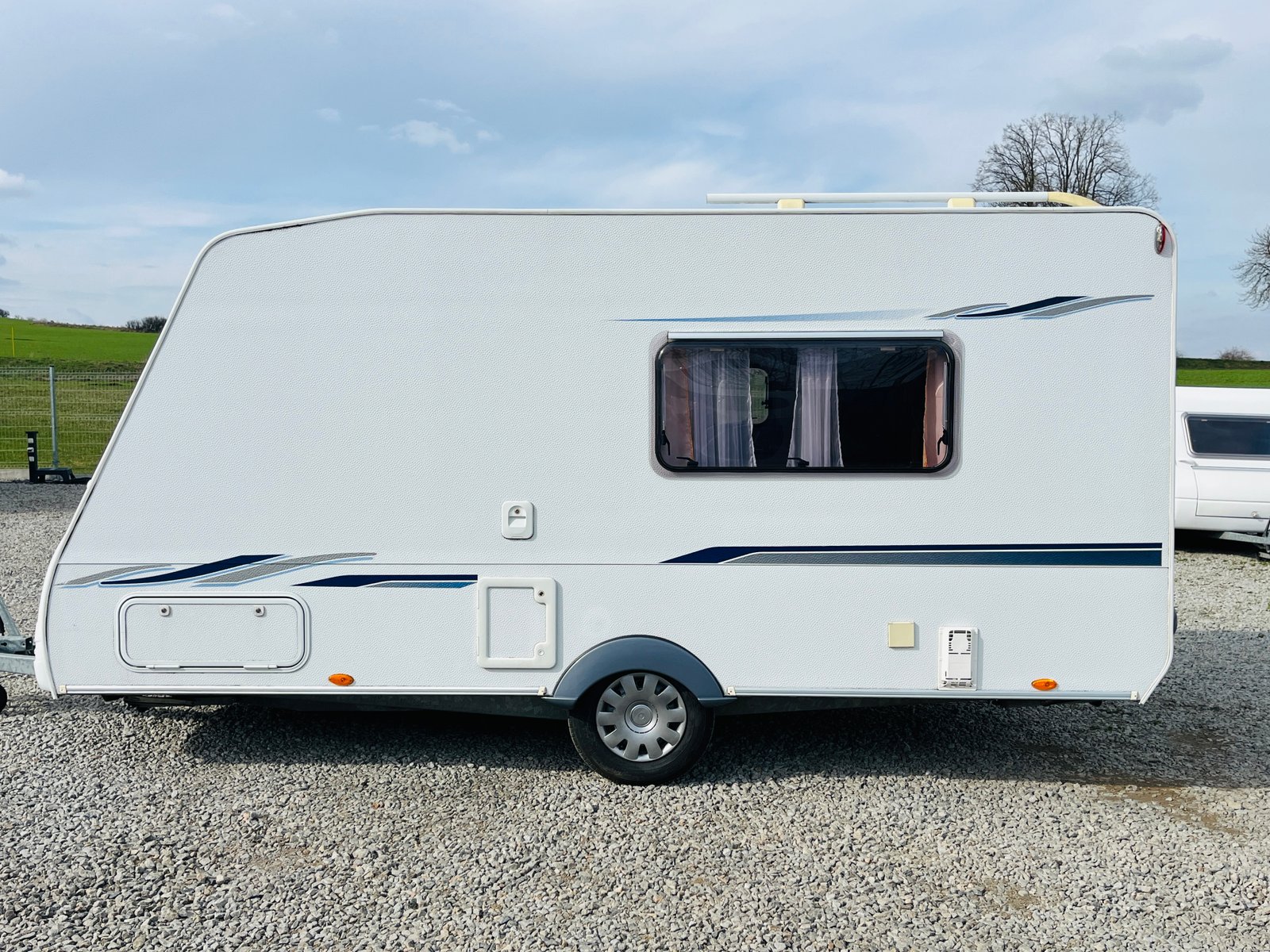 Bílý karavan s bočním oknem a elegantním designem, ideální pro cestování a dobrodružství.