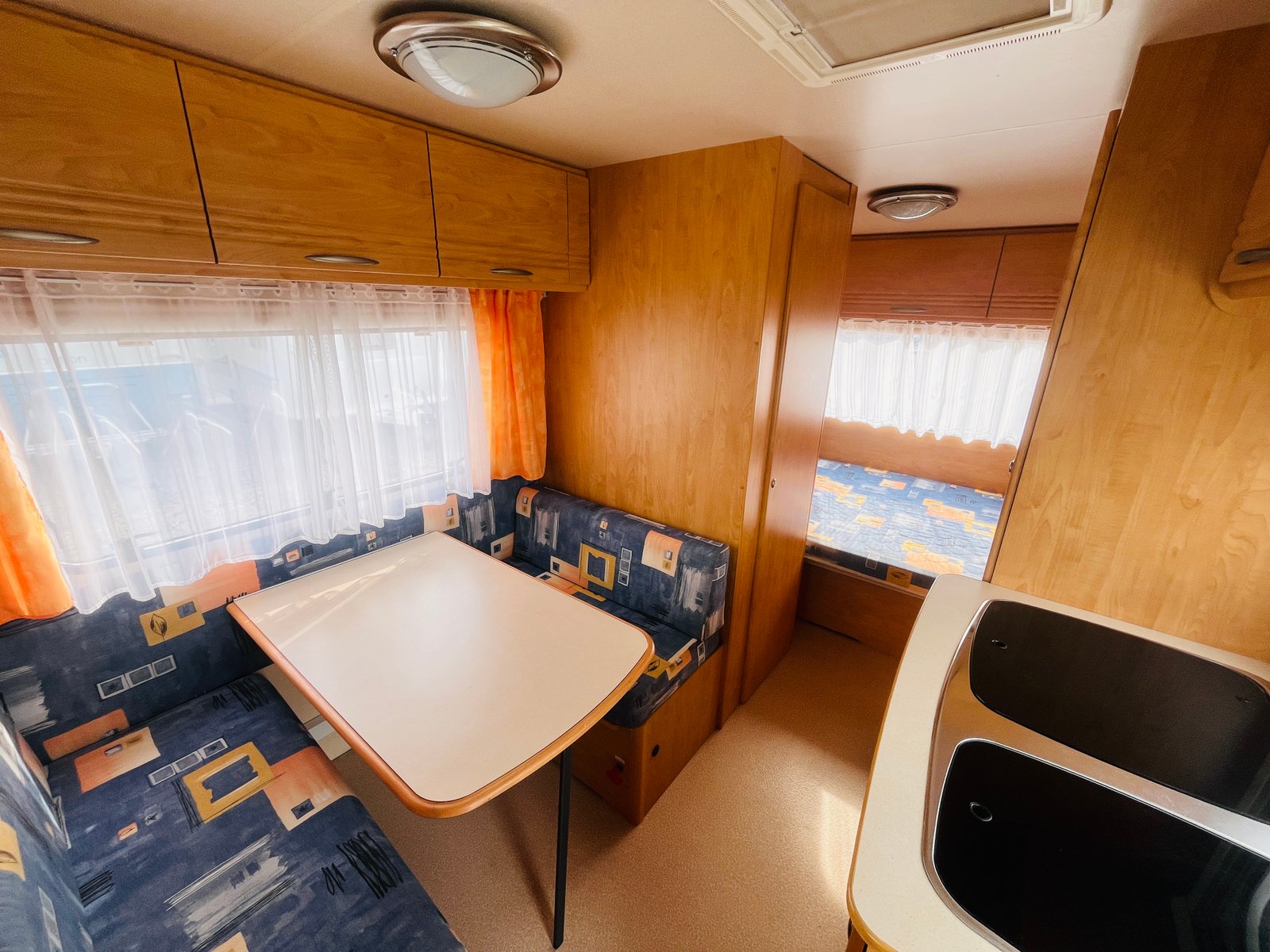 Interiér karavanu s dřevěnými prvky a jídelním stolem. Ideální pro pohodlné cestování.