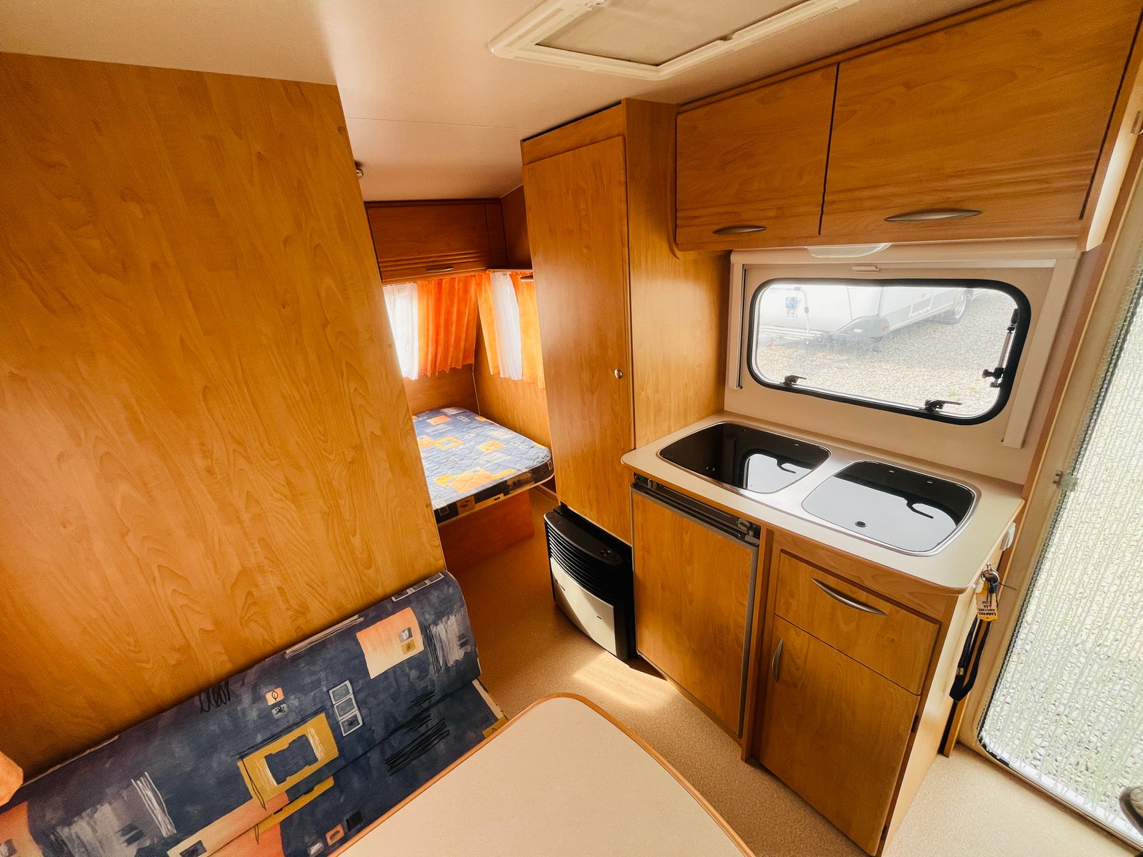 Interiér karavanu s kuchyňským koutem a lůžkem. Ideální pro pohodlné cestování a odpočinek.