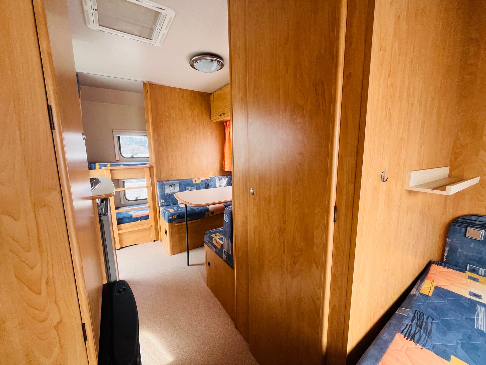 Interiér karavanu, dřevěné obložení, pohodlné sezení a stůl, ideální pro odpočinek.