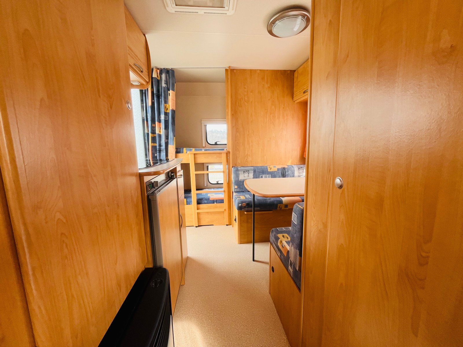 Interiér karavanu s dřevěnými prvky a posedem, ideální pro pohodlné cestování.