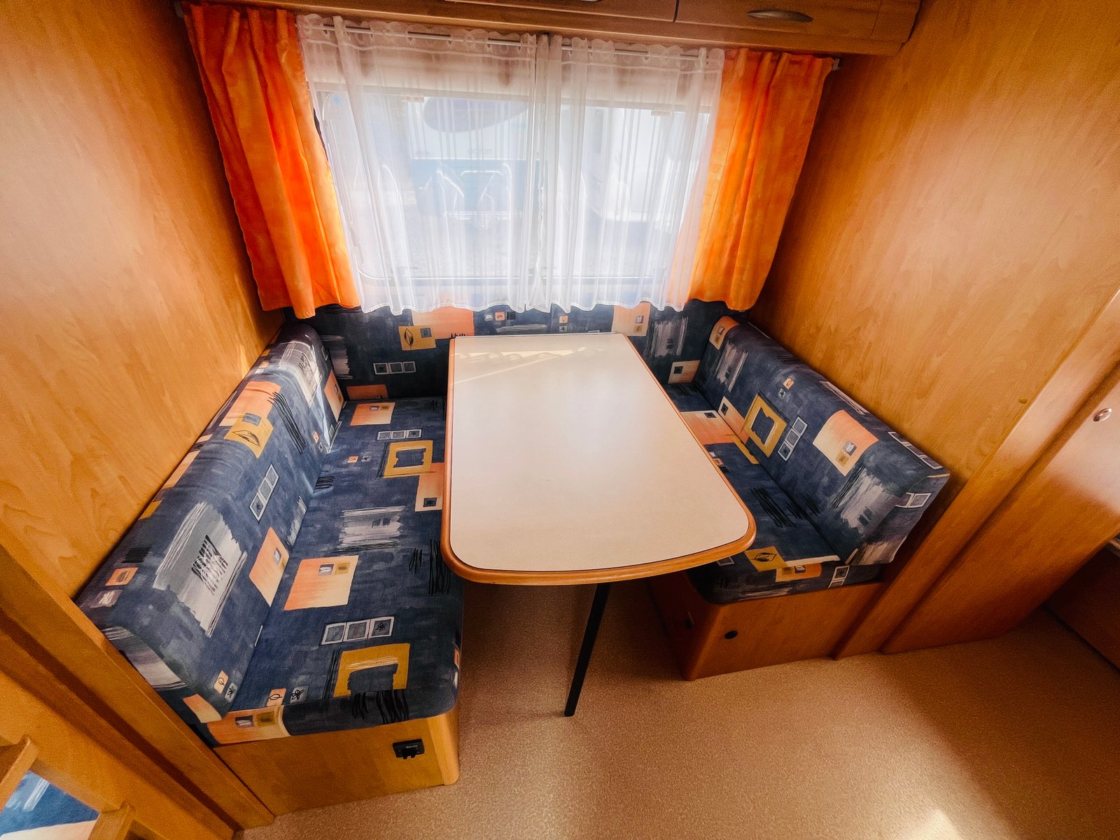 Interiér karavanu s útulným sezením a stolem, ideální pro odpočinek a rodinné chvíle.